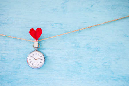 Vintage watch hanging on rope with red heart clip on blue texture background, valentine concept background, love and romance, heart timeの写真素材