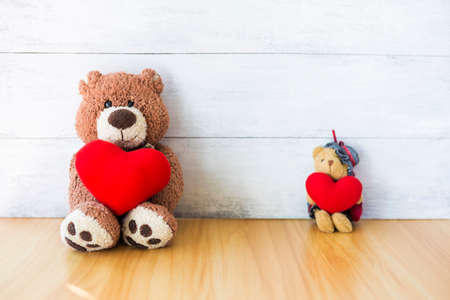 Old teddy bear holding red heart sitting with blurred background, Happy valentine day, love and romance conceptの写真素材