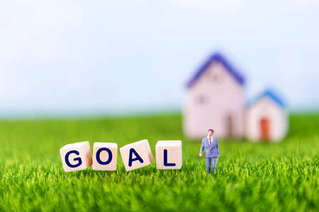 Miniature business man with goal word on wooden cube on green grass with space on blurred background, business conceptの写真素材