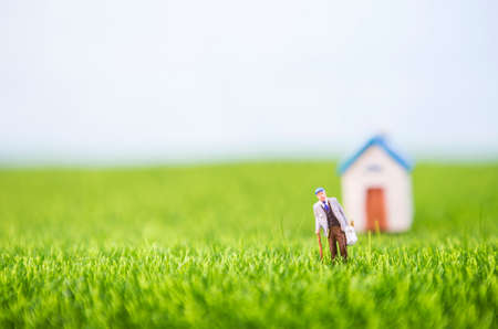 Miniature elderly man carry grocery bag walking in the field with space on blurred house background, selective focus, retired conceptの写真素材