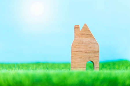 Wooden house model on green grass with space on blurred blue background, property and real estate business concept, summer houseの写真素材