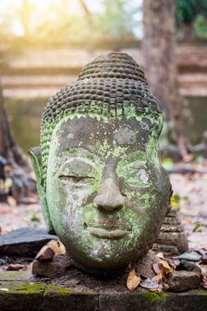 Closeup ancient buddha head over blurred background with vintage warm light, Asian culture, outdoor day light, temple in Thailandの写真素材