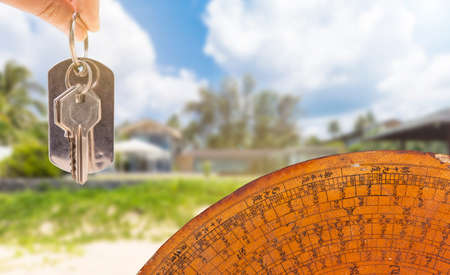 House key in girl hand with ancient feng shui compass over blurred house background, house feng shui