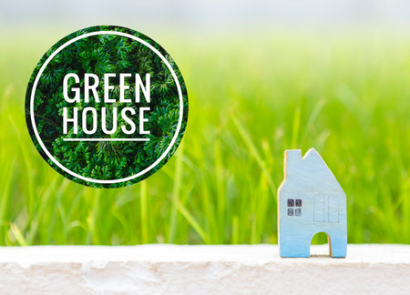 Green house banner with blue wooden house over blurred beautiful green grass background, outdoor day light, house loan or property business concept, new eco houseの写真素材