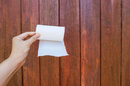 White toilet paper roll in girl hand with space on wood background, cleaning product