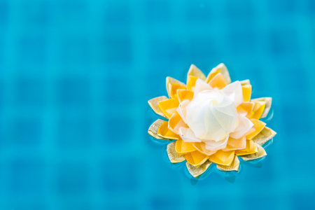 Handmade yellow ribbon flower floating on blue water, craft idea lotus flower made from plastic ribbonの写真素材