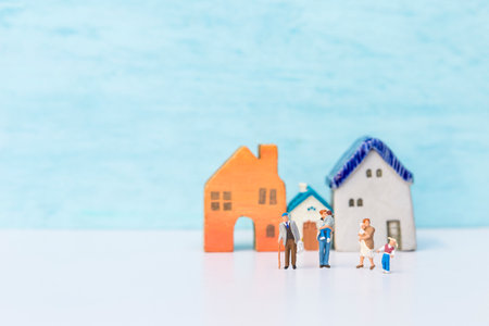 Miniature family in front of vintage hosue model over blurred blue background, family house, property business, life insuranceの写真素材