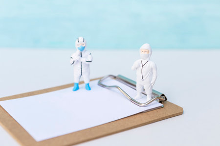 Miniature doctor and nurse in PPE suit standing on paper clipboard, medical report and check list concept, scientist wearing protection suite to protect against coronavirus covid-1の写真素材