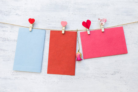 Blank color paper card hanging on rope with heart shape clip on white wood background, valentine...
