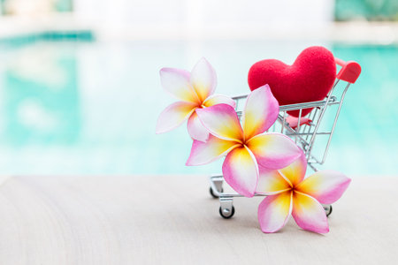 Beautiful plumeria flower with red heart in shopping cart over blurred background, tropical summer, love and romanceの写真素材