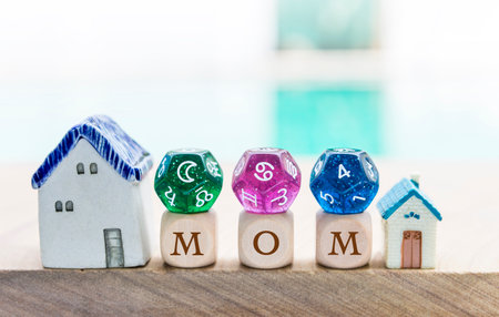 Mom text on wooden cube with divination dice and miniature home over blurred background, fourth house in astrology with moon sign and cancer zodiac sign diceの写真素材