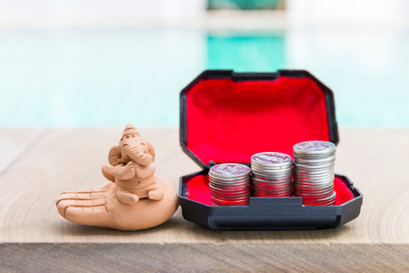 Ganesh clay sculpture with coins stack in treasure box over blurred background, success wealth and luckの写真素材