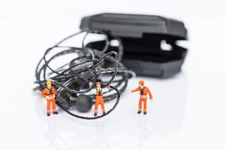 Tangled earphones cable with miniature worker isolate on white background, worker fixing messy wire