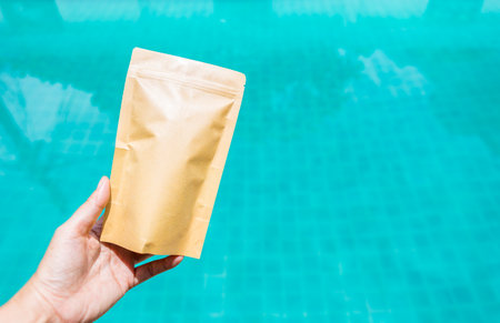 Brown kraft paper bag with zip lock in girl hand over blurred water background, eco friendly...