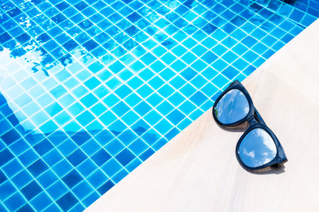 Sunglasses with sky reflection on swimming pool edge with space on blue water background, summer outdoor day ligth, summer eyewear fashionの写真素材