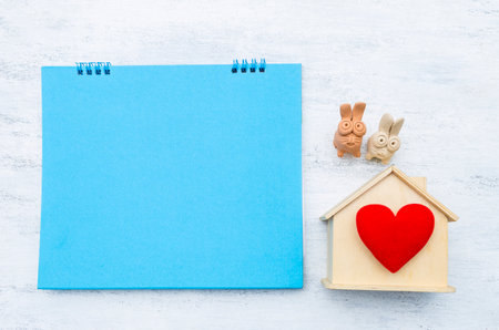 Blank blue card with wooden house model and red heart with rabbit clay sculpture on white background, buy new hosue, property investment, real estate businessの写真素材
