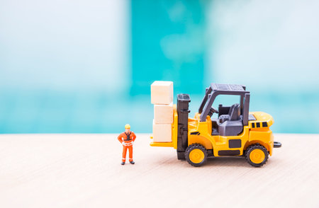 Miniature worker in safety suite with forklift truck and wooden cubes, cargo industry conceptの写真素材