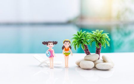 Two miniature girl in swimwear with coconut tree over blurred swimming pool background, summer season and holiday concept, fun outdoor activity, women fashionの写真素材