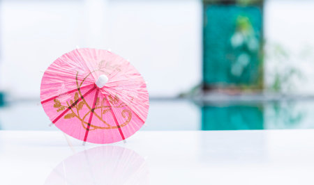 Pink paper umbrella on swimming pool edge with space on blurred background, summer outdoor day light, tropical summer conceptの写真素材