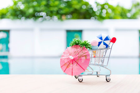 Summer decoration item in shopping card on swimming pool edge, outdoor day light, summer sale, Paper umbrella with coconut tree and ice cream in shopping cartの写真素材