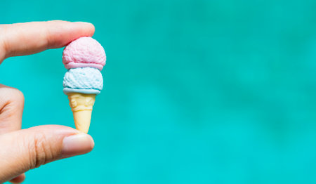 Mini ice cream cone in girl hand with space on blurred blue water background, summer outdoor day light, welcome summerの写真素材
