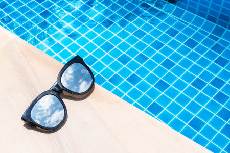 Sunglasses on swimming pool edge with space on blue water background, summer outdoor day light,...