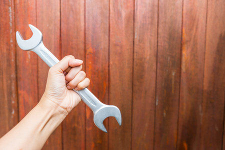 Girl hand holding open end wrench with space on wood background, quality open end spanner, hand toolsの写真素材