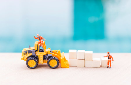 Miniature worker in safety suite with front loader truck and wooden cubes, cargo and logistic industry conceptの写真素材