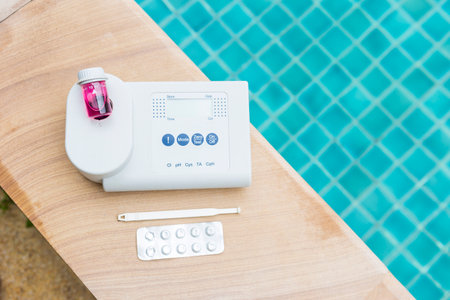 Quality water analysis tool on swimming pool edge with space on water background, measure chlorine and pH, pH testing with water photometer and reagent tableの写真素材