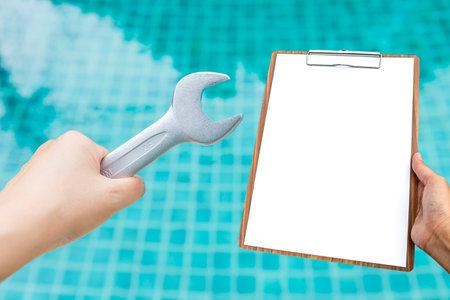Girl hand holding wrench and blank report paper on clipboard over blurred swimming pool water background, pool maintenance service or reportの写真素材