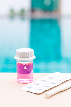 Pool water in glass vials with pH table reagents and stirring rod on swimming pool edge, water analysis tools, free chlorine testの写真素材