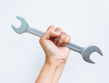 Hand holding double open end wrench on white cement wall background, quality tool industryの写真素材