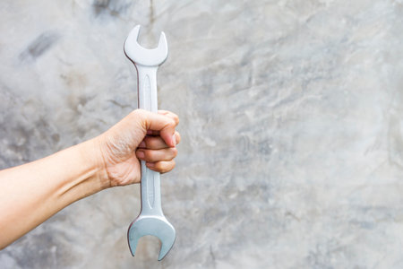 Girl hand holding open end wrench with space on grey cement wall background, quality open end spanner, hand toolsの写真素材