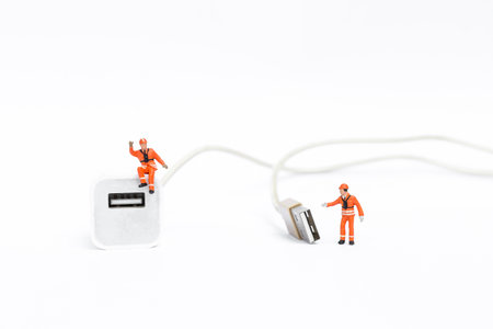 Miniature worker in safety suit with USB charging cable, standard charging port for electronic devicesの写真素材
