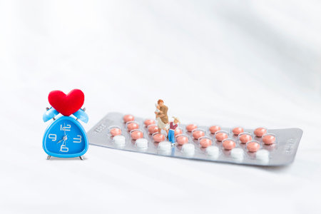 Miniature women with kids on birth control pill with red heart on alarm clock on white bed sheet background, health care and medical concept, women healthの写真素材