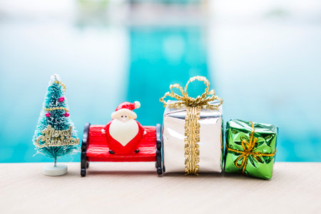 Christmas background idea, Santa doll on red bench with gift box and Christmas tree over blurred...