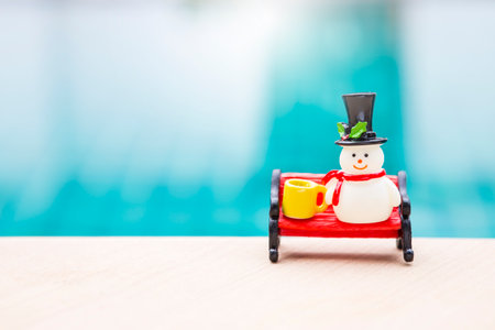 Snowman doll with coffee cup on red bench over blurred blue water background, Christmas background idea, outdoor day light, festive season conceptの写真素材