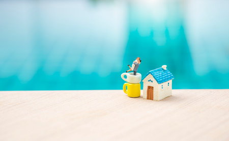 Miniature couple in coffee cup with miniature house on blue water background, outdoor day light, valentine card background ideaの写真素材