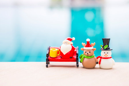 Christmas background idea, Santa doll on red bench with reindeer and snowman over blurred background, outdoor day light, festive season conceptの写真素材