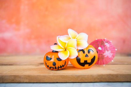 Plumeria flower with Halloween pumpkin and paper umbrella with space on orange cement wall, tropical Halloween card background ideaの写真素材