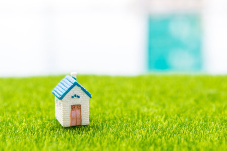 Miniature house model on green grass with space over blurred outdoor garden background, property and real estate business concept, property investment, retirement home, house insurの写真素材