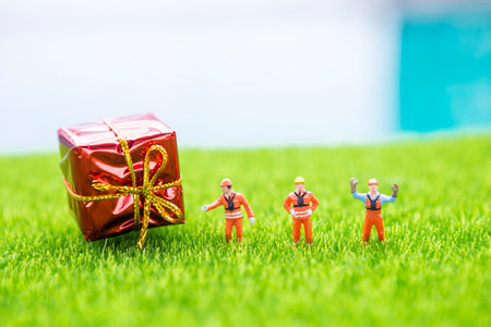 Miniature worker with red gift box on green grass with space on blurred background, outdoor day light, Christmas and new year holiday conceptの写真素材