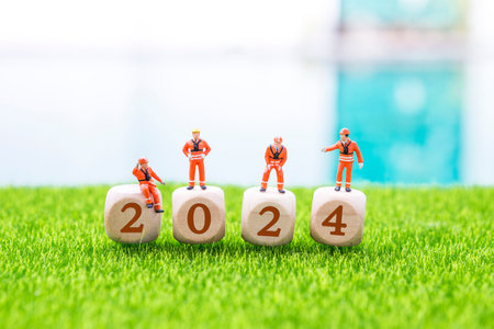 New year 2024 concept, miniature worker on wooden cube with number on green grass with space on blurred background, new year celebration and holidayの写真素材