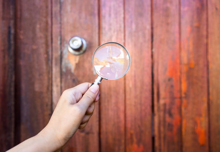 Girl hand holding maginifying glass in front of wooden door, investigate and research, outdoor day lightの写真素材