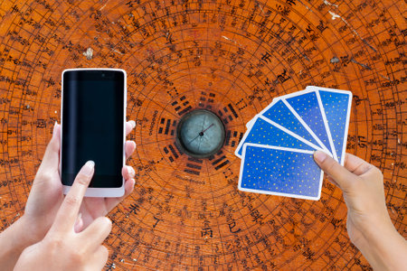 Smartphone and tarot card in girl hand over Feng Shui compass plate background, online fortune telling, fate and believe conceptの写真素材