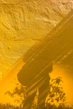 Human shadow on the yellow cement wall, vertical style, outdoor day light, artistic background