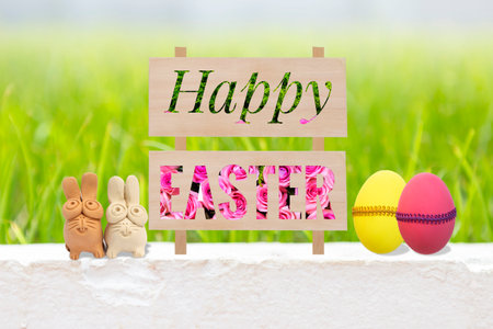 Happy Easter sign with flower and green leaves pattern on cement wall with clay rabbit and easter...