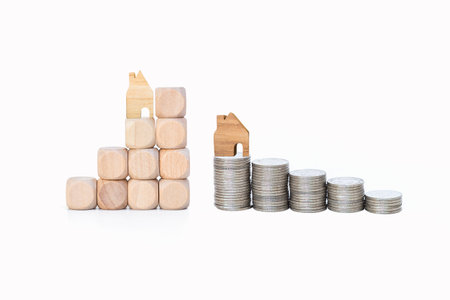 Miniature house on wooden cubes and coin stack isolate on white background, property and real estate investment conceptの写真素材