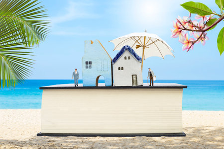 Miniature house with miniature business man and old man carry grocery bag on thick book over tropical beach background, property and real estate investment concept, elderly house pの写真素材