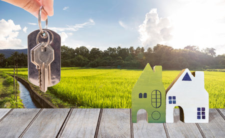 Wooden house model with house key in girl hand over rice field background, buy property in countryside, real estate business concept